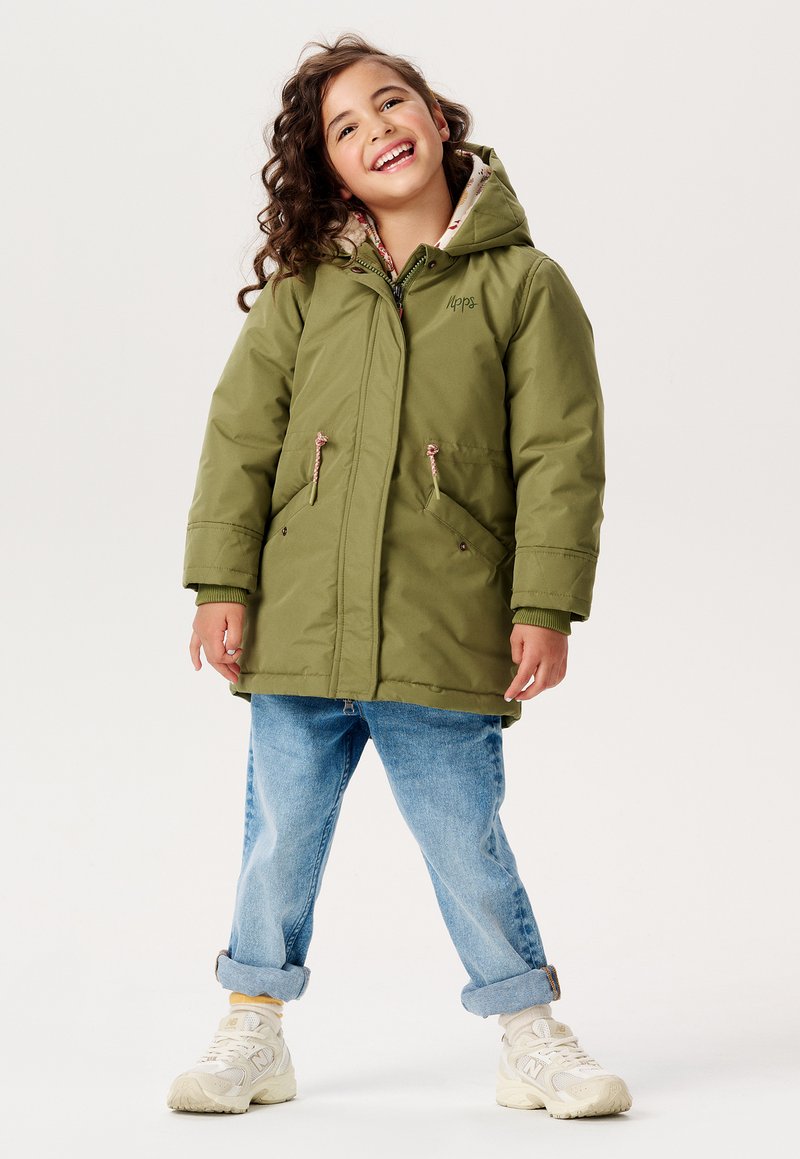 Olivenfarvet, hætteparka med snor i taljen og lommer. Foret med mønstret stof. Sammen med opsmøget blå jeans og lyse sneakers.