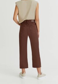 Jean marron taille haute, jambes larges et raccourcies, avec poches arrière, confectionné dans un mélange de coton pour plus de confort. Associé à des chaussures beiges à enfiler.