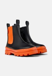Bottes chelsea noires en cuir avec des panneaux élastiques latéraux orange, semelles en caoutchouc orange robustes et languettes pour un enfilage facile.