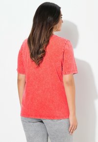 Rode, korte mouwen t-shirt met een vervaagde, versleten uitstraling. Ronde halslijn en gestikte accenten op de mouwen en onderkant. Gekozen in combinatie met grijze broek.