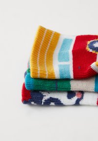 Bunte gestrickte Socken gestapelt: Die oberste Socke in Gelb- und Rotstreifen, die mittlere in Grün und die untere mit einem Muster auf marineblauem Hintergrund.