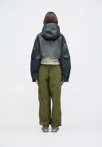 Krajša siva vodoodbojna jakna s kapuco, kombinirana z ohlapnimi olivno zelenimi cargos hlačami in sivimi pohodnimi čevlji. Ponaša se z žepi in kontrastnimi črtami.