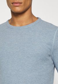 Světlomodré tričko s dlouhým rukávem a kulatým výstřihem vyrobené z texturované látky, s žebrovaným límcem a švy v těsném střihu.