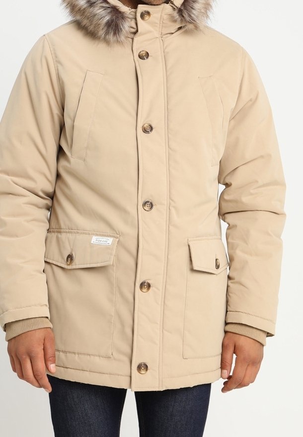 Parka beige isolée avec une capuche bordée de fourrure, boutons à l'avant, deux poches poitrine, et poignets côtelés. Matière lisse avec une finition mate.