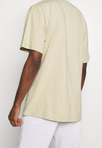 Beige bomulds T-shirt med korte ærmer og lige snit, der viser en glat tekstur og minimalistisk design på ryggen.