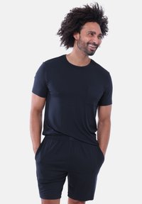 Maglietta nera a maniche corte con tasca, abbinata a pantaloncini neri coordinati. Il tessuto sembra morbido e liscio, con una cintura elastica.