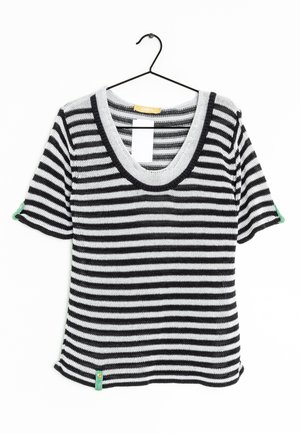 Top de punto a rayas en blanco y negro con un escote amplio y mangas cortas. Cuenta con una etiqueta de acento verde en el dobladillo. Textura ligera.