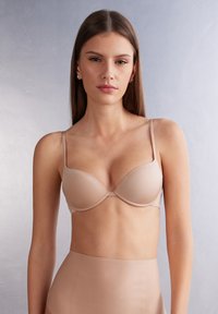 Beige padded bra with adjustable straps, smooth texture, and a seamless design. Accompanied by high-waisted beige bottoms.