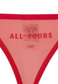 Culotte string rouge en tissu mesh, avec une ceinture unie rouge contrastante et le texte « ALL YOURS » imprimé en lettres majuscules.
