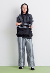Black zip-up hoodie with gray stripes on sleeves, paired with gray camo-patterned wide-leg pants. Model wearing black athletic shoes.