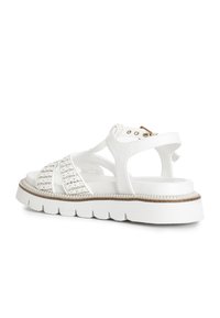 Bílé sandály s pletenými pásky, masivní podrážkou s texturovanou gumou a detaily zlatého tónu na pásku kolem kotníku.