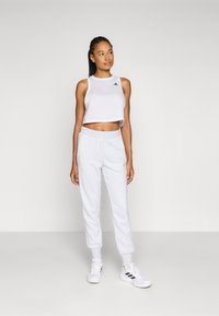 Top corto blanco con logo negro, combinado con pantalones de chándal grises claros y zapatillas blancas. Tejido suave con un ajuste relajado.