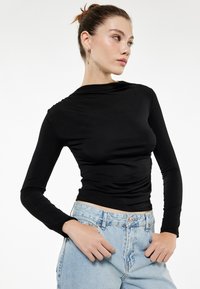Top de manga larga negro con un diseño elegante y ajustado, hecho de un material suave. Presenta un escote redondo y detalles ligeramente fruncidos en la cintura.