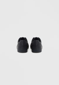 Black sneakers with a smooth matte finish, rounded shape, and cushioned ankle support. Features a textured rubber sole and lace-up design.