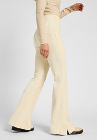 Pantaloni svasati color crema realizzati in tessuto a coste, con vita alta e fessure laterali all'orlo.