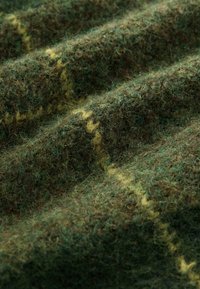 Brown and green wool fabric with a soft, fuzzy texture, featuring a subtle yellow pattern and waves of draped folds.