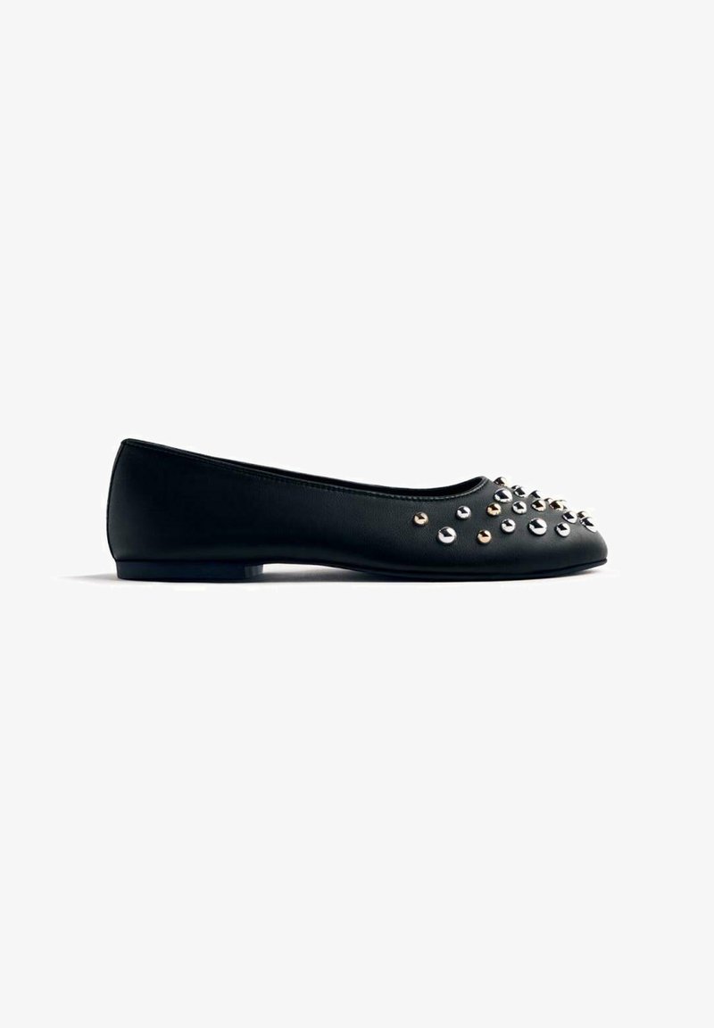 Bailarina de cuero negro con tachuelas plateadas y doradas en la parte delantera, con forma redondeada y tacón bajo. Textura suave.