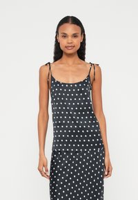 Zwarte cami top met witte stippen, gemaakt van lichtgewicht stof met verstelbare spaghetti bandjes. Heeft een gladde textuur.