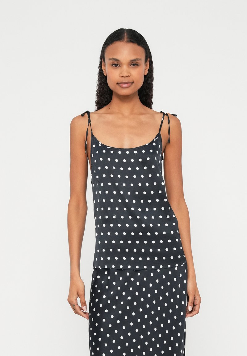 Zwarte cami top met witte stippen, gemaakt van lichtgewicht stof met verstelbare spaghetti bandjes. Heeft een gladde textuur.