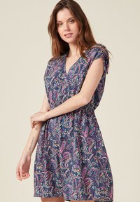 Kurzarmkleid in Marineblau mit einem lebhaften Paisley-Muster in Violett-, Grün- und Weißtönen; V-Ausschnitt und geraffte Taille.