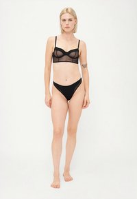 Zwarte doorschijnende bralette met beugel en verstelbare bandjes, gecombineerd met een zwarte high-cut string. Beide hebben een gladde textuur en minimale details.