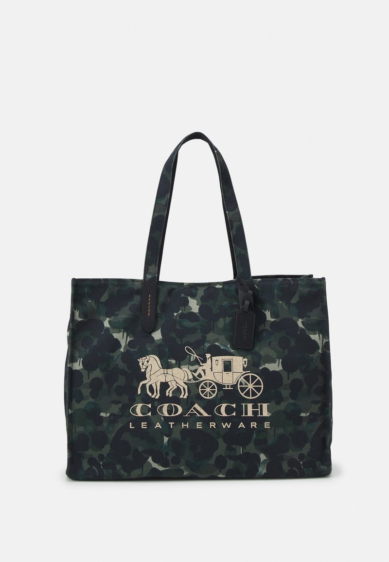 Sac fourre-tout à motif camouflage vert foncé avec deux anses, présentant un graphisme de calèche tirée par des chevaux et le texte "Coach Leatherware" sur le devant.