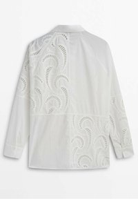 Chemise blanche boutonnée avec un délicat motif en dentelle ondulée, manches longues et col classique. Texture lisse.