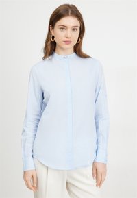 Camicia azzurra chiaro, a maniche lunghe, con chiusura a bottoni e colletto alla cinese. Realizzata in un tessuto leggero e morbido. Leggero lucido.