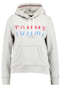 Jasnoszara bluza z kapturem z przednią kieszenią, białymi sznurkami i napisem "TOMMY" wydrukowanym na klatce piersiowej w czerwonych, białych i niebieskich literach.