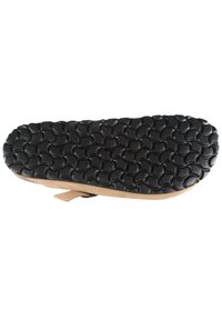 Suela de sandalia con patrón de relieve negro y curvado, y tirante beige parcialmente visible debajo, sobre fondo blanco.