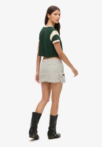 Groen cropped topje met crèmekleurige korte mouwen, gecombineerd met een grijze denimrok met een rafelige zoom en cargozak. Zwarte kniehoge laarzen.