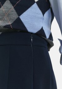 Close-up van een persoon die een marineblauwe rok met een zijrits en een argyle-patroon trui in tinten blauw en grijs draagt.