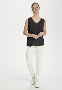 Haut sans manches noir avec un col en V et un détail de plis subtil, assorti à un pantalon blanc ajusté et des baskets blanches. Texture de tissu lisse.