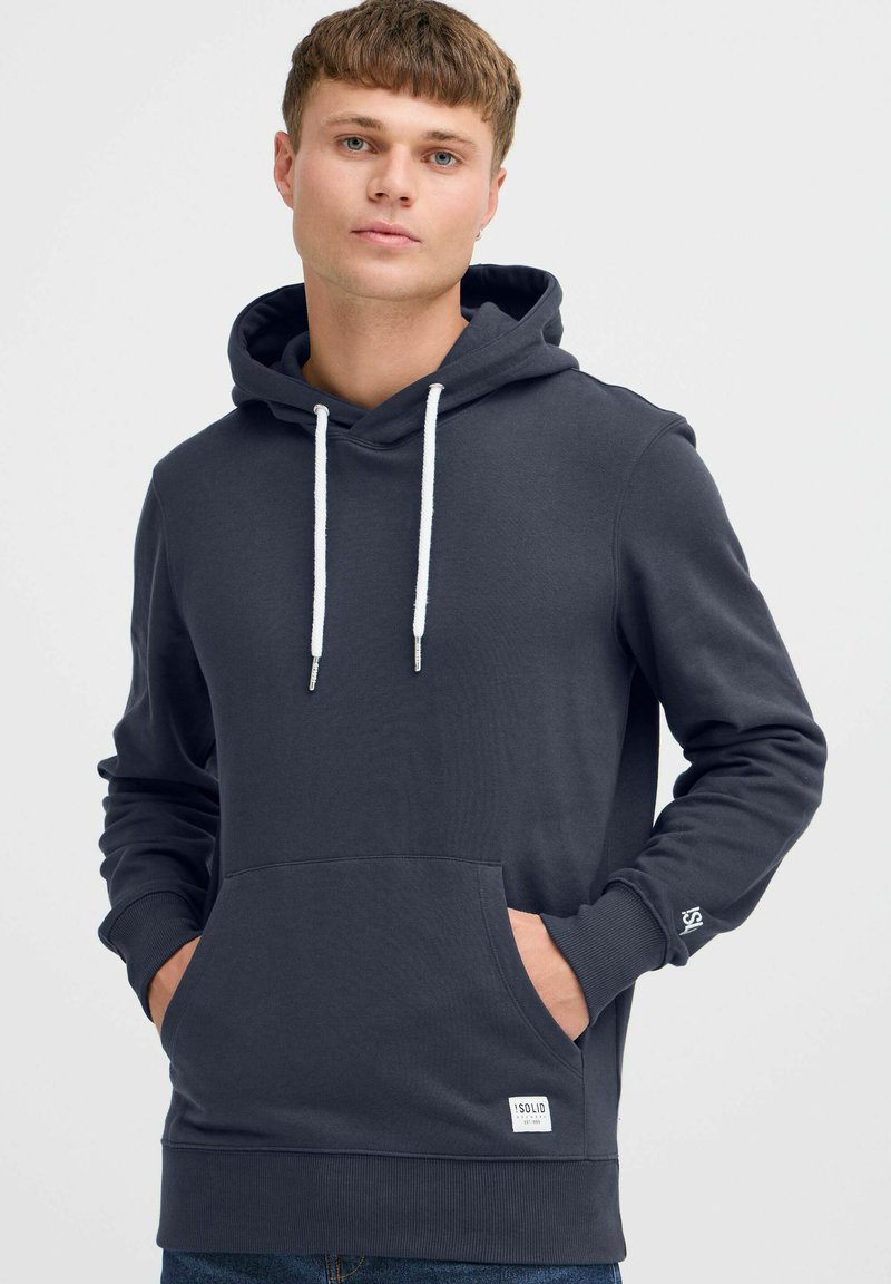 Donkergrijze hoodie van zacht materiaal, met een voork pocket, witte trekkoorden, geribde manchetten en een klein logo label.