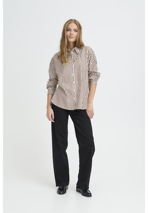 Brun och krämrandig knapp-up skjorta, oversized passform, upprullade ärmar, i kombination med svarta vida byxor och loafers, mot en enhetlig bakgrund.