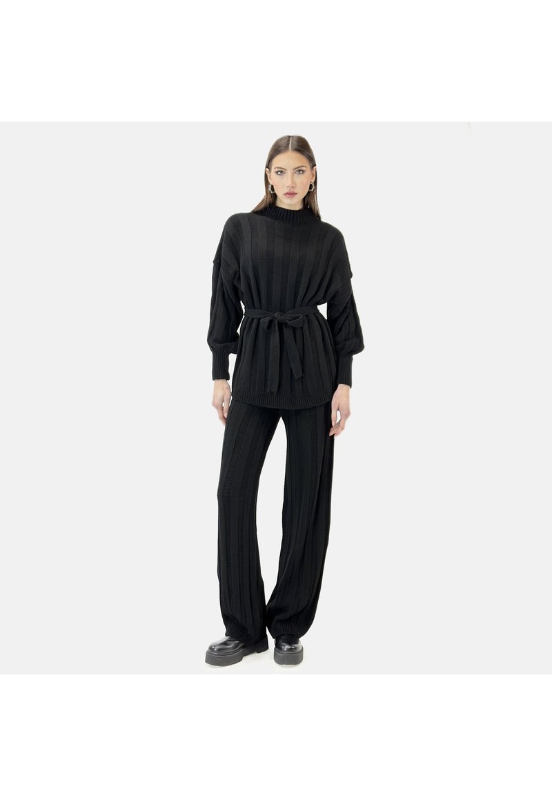 Conjunto de punto negro con un diseño acanalado, cuello alto y cintura atada, combinado con pantalones de corte holgado y zapatos de plataforma.