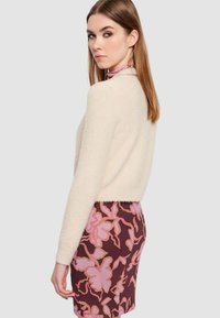 Maglione crema soffice con maniche lunghe abbinato a una gonna a fiori marrone con accenti rosa. Texture liscia e vestibilità moderna.