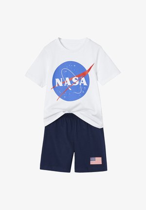 Weißes T-Shirt mit kurzen Ärmeln und blauem NASA-Logo sowie marineblaue Shorts mit einem kleinen amerikanischen Flaggenaufnäher am linken Bein.