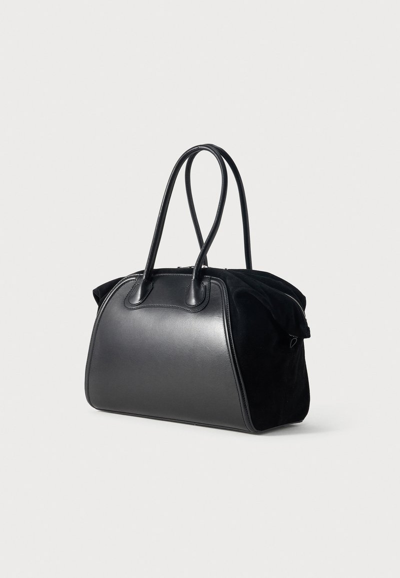 Black leather and suede handbag with rounded rectangular shape and two thin handles standing upright against a plain background.