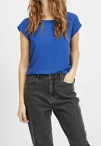 Blå kortärmad topp med en texturerad yta, matchad med högmidjade svarta jeans med avslappnad passform och klassisk femficksdesign.