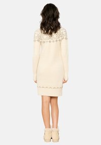 Vestito di maglia crema con yoke a fantasia, maniche lunghe e lunghezza a metà coscia. Abbinato a stivali alla caviglia foderati in pelliccia beige.