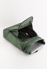 Grön laptopryggsäck med en slät yta, dragkedjestängning och justerbara axelremmar. Öppen och visar vadderat inre och fack.