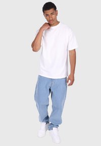 Hvid bomulds t-shirt parret med lyseblå baggy jeans og hvide sneakers. T-shirten har korte ærmer og en rund udskæring.