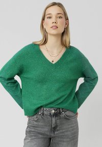 Pull vert à col en V en tricot doux et texturé. Doté de manches longues et d'une coupe décontractée, associé à un jeans en denim gris.