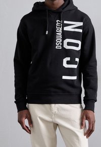 Sudadera negra con capucha con texto blanco en negrita que dice "DSQUARED?" y "ICON" en posición vertical. Confeccionada con tejido suave y texturizado, con capucha ajustable con cordón.