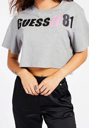 Szara krótka koszulka z nadrukiem "GUESS//81" w grubych czarnych i różowych literach. Miękki bawełniany materiał z krótkimi rękawami. Czarne spodnie dresowe.