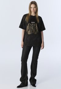 Oversized T-Shirt mit schwarzem Leopardenmuster, featuring einem strukturierten braunen Hasen-Grafik, kombiniert mit schwarzen Schlagjeans mit weißen Nähte-Details.