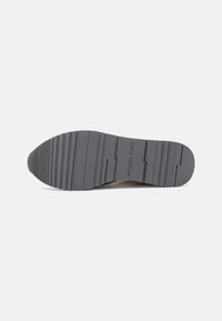 Gray rubber shoe sole featuring horizontal ridges and a textured surface, with "MICHAEL KORS" embossed near the center.