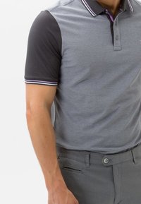 Polo shirt col montant en gris avec des manches courtes noires, présentant de fines accents blancs et violets sur le col. Le matériau semble doux et léger.