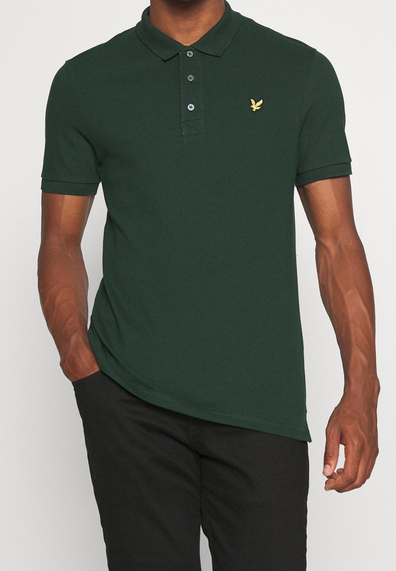 Grünes Poloshirt aus Baumwolle mit einem Drei-Knopf-Verschluss, kurzen Ärmeln und einem kleinen gelben Logo auf der Brust.